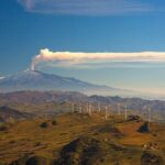 View of windmills and the mount Etna Volcano with smoke. Sicily